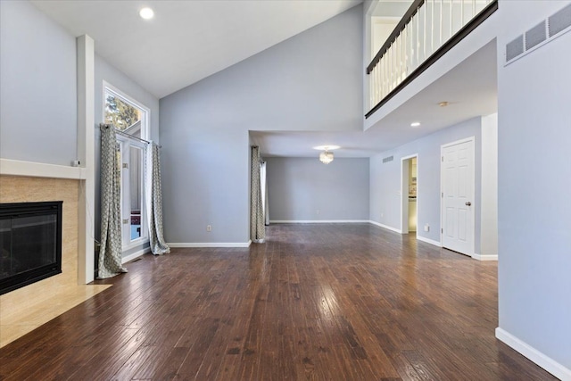 unfurnished living room featuring baseboards, visible vents, a tiled fireplace, dark wood-style floors, and high vaulted ceiling