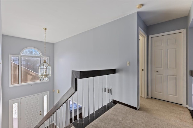 corridor with light carpet, baseboards, an upstairs landing, and a notable chandelier