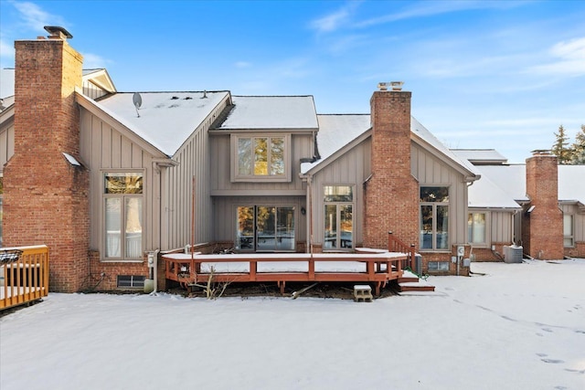 snow covered rear of property with a chimney, visible vents, board and batten siding, central AC, and a wooden deck