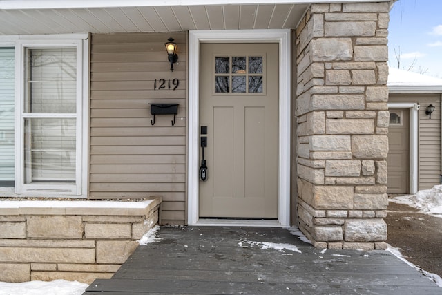 snow covered property entrance featuring stone siding