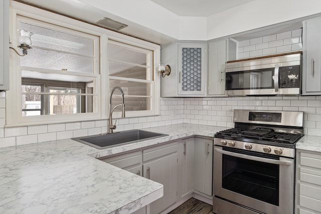 kitchen with stainless steel appliances, gray cabinets, a sink, and tasteful backsplash