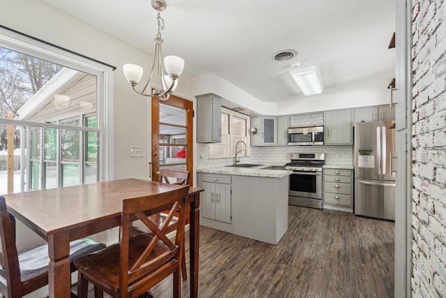 kitchen featuring dark wood-style flooring, stainless steel appliances, tasteful backsplash, gray cabinetry, and a sink