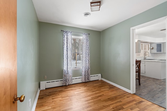 unfurnished room with a baseboard heating unit, a sink, visible vents, baseboards, and light wood-type flooring