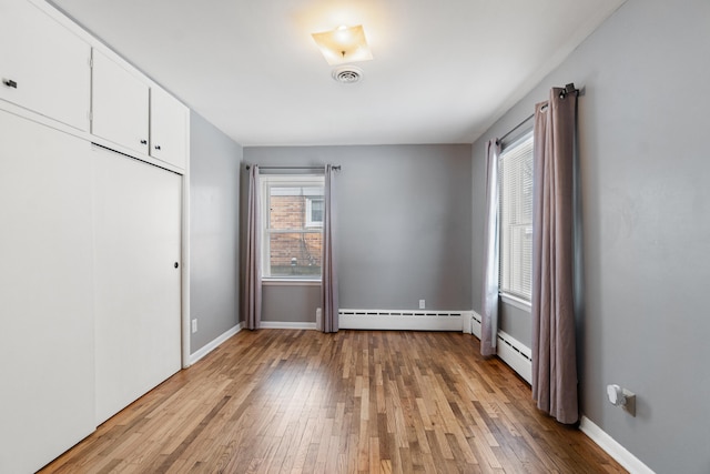 unfurnished bedroom with light wood-type flooring, a baseboard radiator, and baseboards