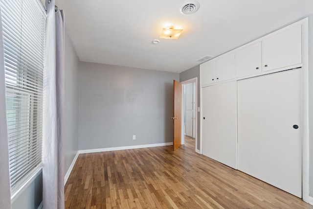 unfurnished bedroom featuring light wood finished floors, baseboards, visible vents, and a closet