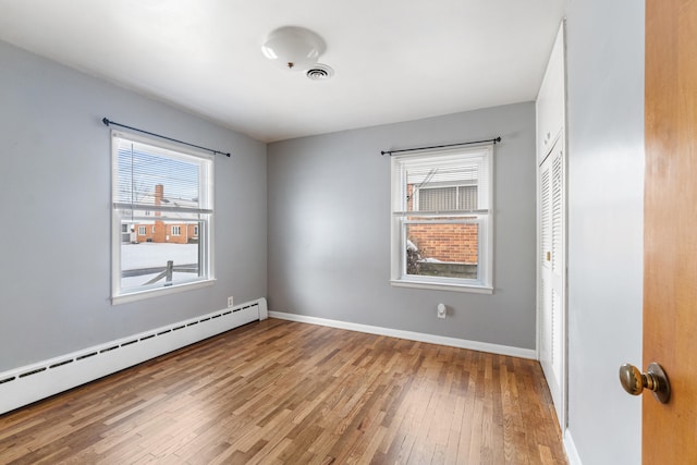 interior space featuring baseboards, visible vents, baseboard heating, and wood finished floors