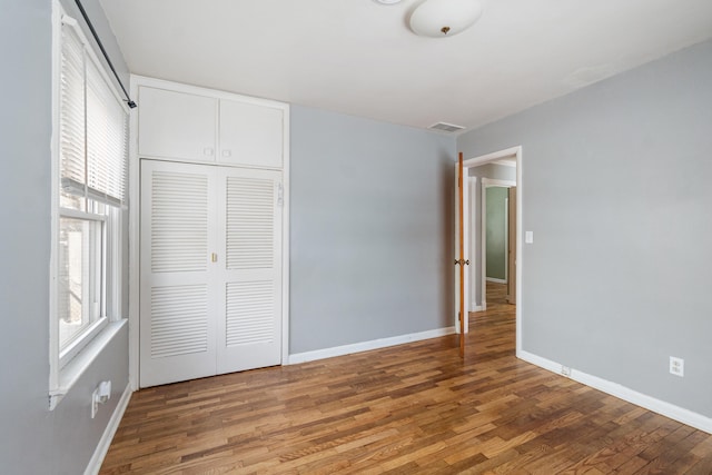 unfurnished bedroom with a closet, visible vents, baseboards, and wood finished floors