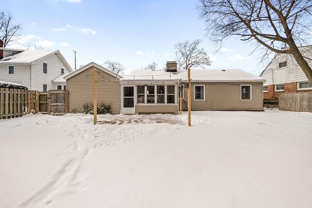 snow covered rear of property featuring fence and a chimney