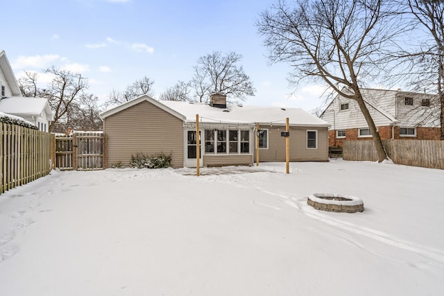 snow covered back of property featuring an outdoor fire pit, a chimney, and a fenced backyard