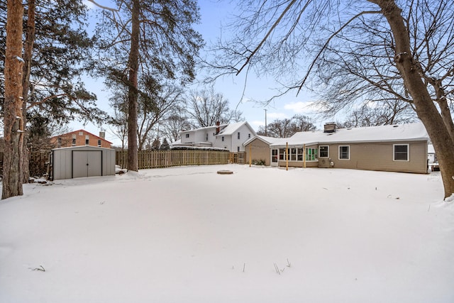 snowy yard featuring fence, a storage unit, and an outdoor structure