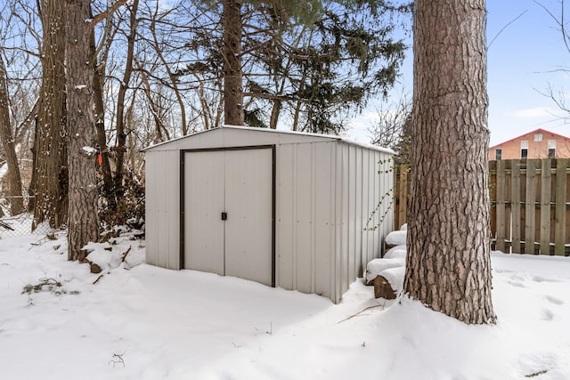 snow covered structure with an outbuilding, fence, and a shed