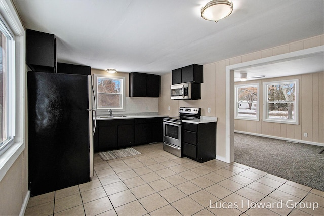 kitchen featuring light colored carpet, light countertops, appliances with stainless steel finishes, a sink, and dark cabinets