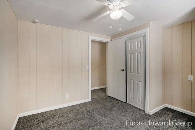 unfurnished bedroom with wood walls, ceiling fan, dark carpet, and a closet