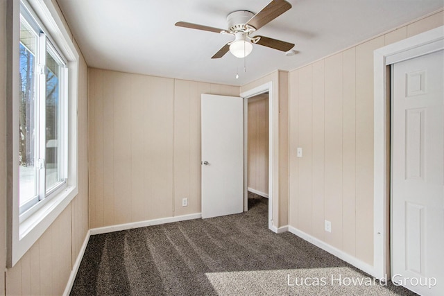 unfurnished bedroom with baseboards, dark colored carpet, and a ceiling fan