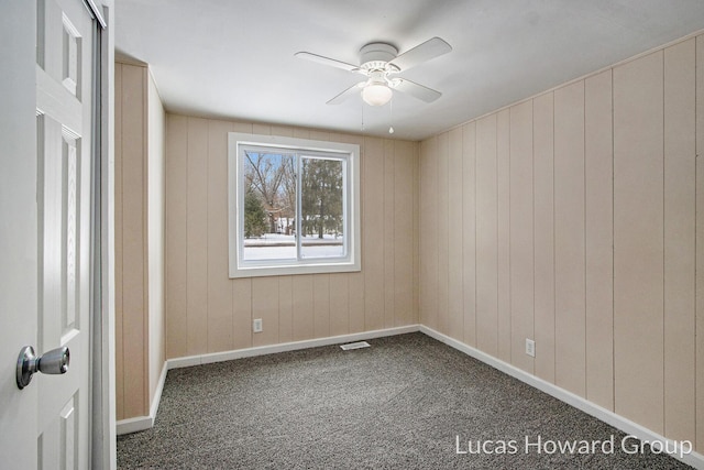 spare room with a ceiling fan, visible vents, dark carpet, and baseboards