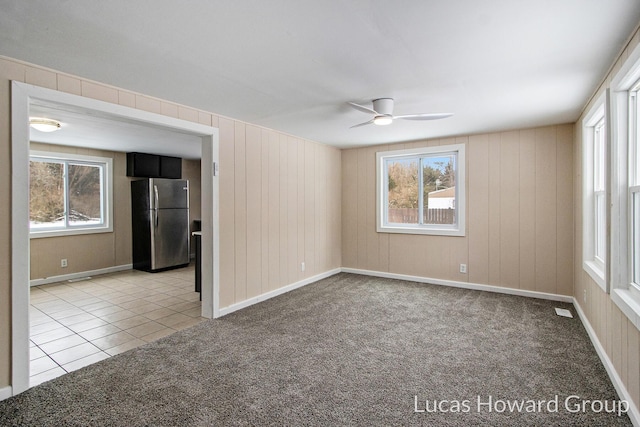 empty room featuring light tile patterned floors, visible vents, a ceiling fan, and light colored carpet