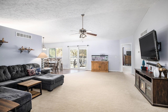 living room featuring ceiling fan, a textured ceiling, light carpet, visible vents, and baseboards