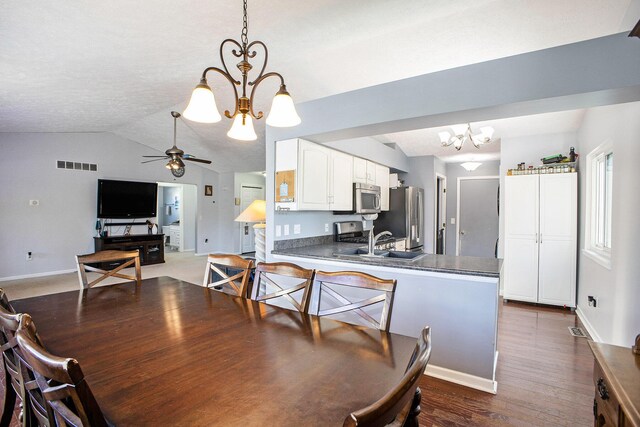 dining space featuring dark wood finished floors, visible vents, vaulted ceiling, baseboards, and ceiling fan with notable chandelier