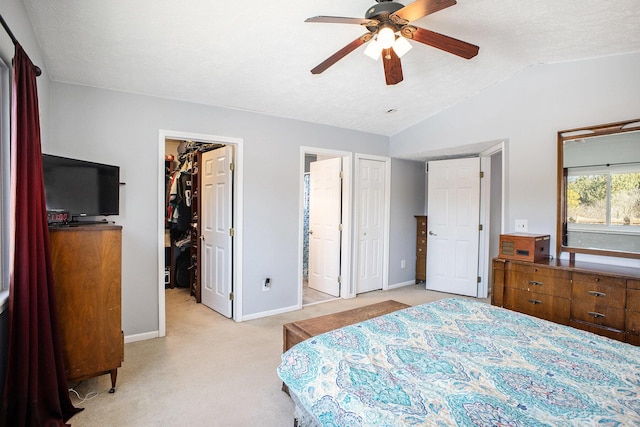 bedroom featuring a walk in closet, light colored carpet, vaulted ceiling, ensuite bath, and baseboards