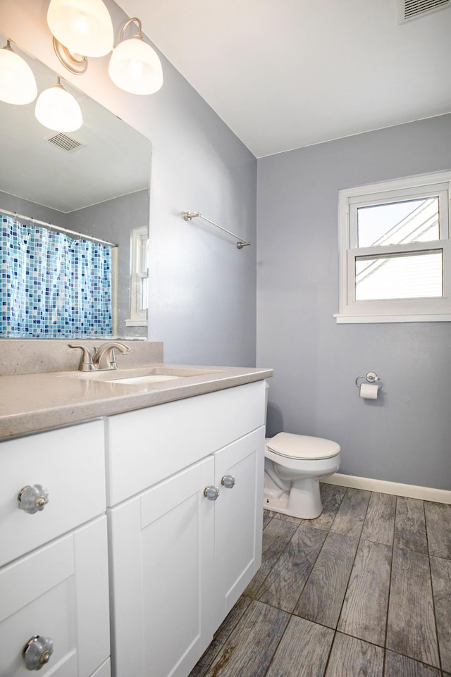 bathroom with wood finish floors, visible vents, toilet, vanity, and baseboards