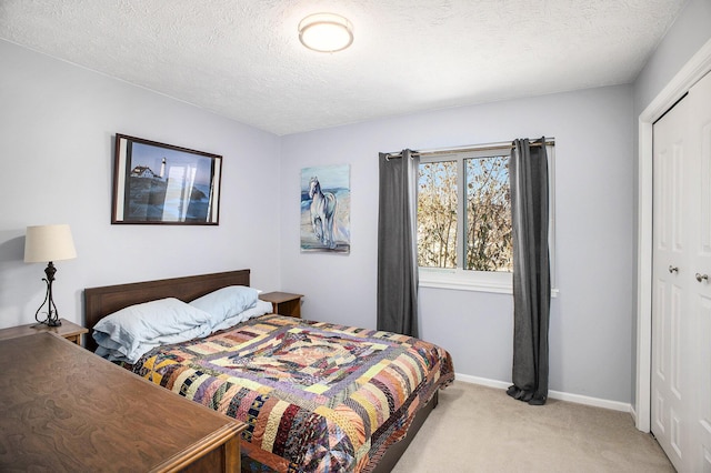 bedroom with a closet, light carpet, a textured ceiling, and baseboards