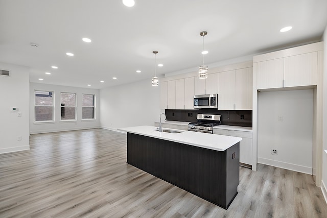 kitchen with decorative light fixtures, light countertops, appliances with stainless steel finishes, a kitchen island with sink, and a sink