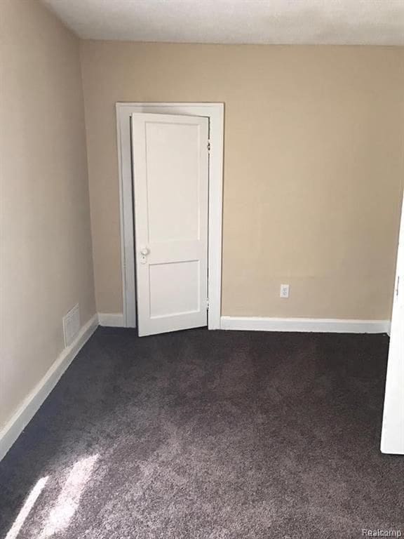 empty room featuring visible vents, dark carpet, and baseboards