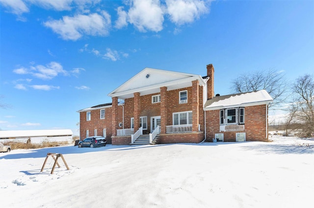 snow covered house featuring a chimney and brick siding