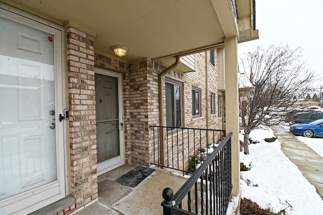 snow covered property entrance with a garage and brick siding