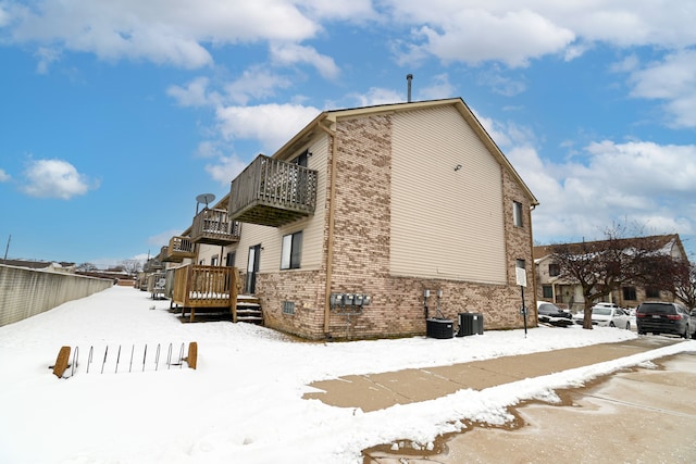 view of snowy exterior featuring a balcony, a residential view, fence, and brick siding