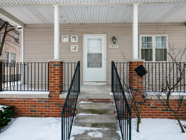 snow covered property entrance with covered porch and brick siding