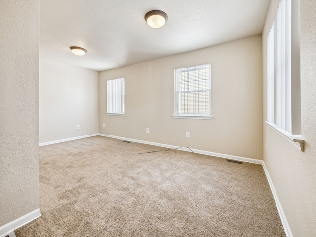 empty room featuring a textured ceiling, a textured wall, carpet floors, visible vents, and baseboards