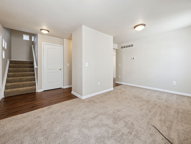 carpeted empty room featuring stairs, visible vents, and baseboards