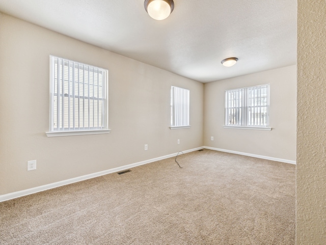 empty room featuring carpet floors, visible vents, a textured ceiling, and baseboards