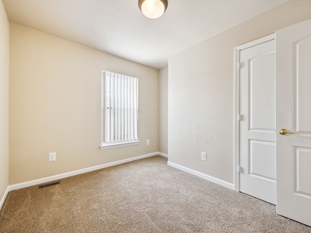 spare room with carpet flooring, visible vents, and baseboards