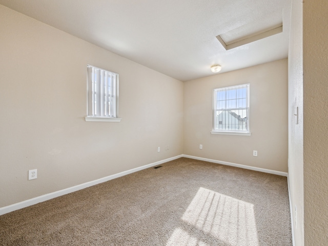 carpeted empty room featuring attic access, visible vents, and baseboards