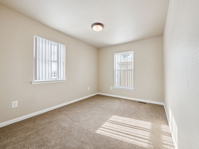 spare room with carpet floors, visible vents, and baseboards