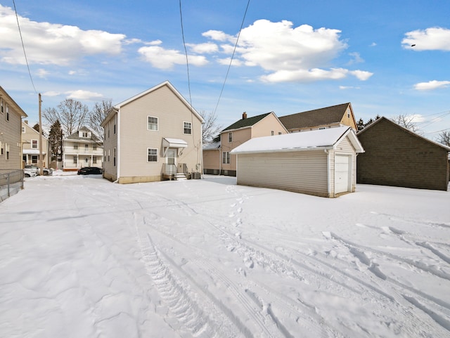 snow covered back of property featuring a garage, an outbuilding, and a residential view