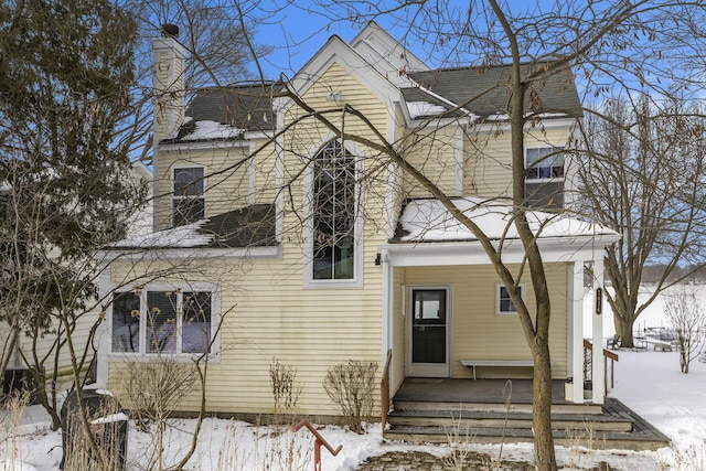 view of front of home featuring roof with shingles, a porch, and a chimney