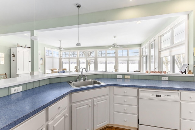 kitchen featuring pendant lighting, dark countertops, white cabinetry, white dishwasher, and a sink