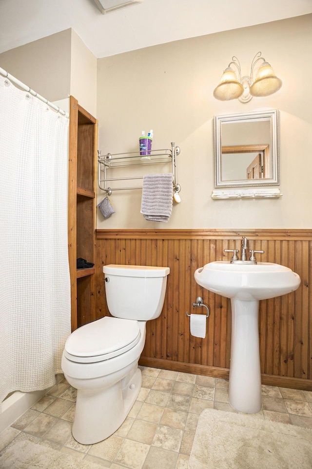 bathroom featuring stone finish flooring, a wainscoted wall, wooden walls, and toilet