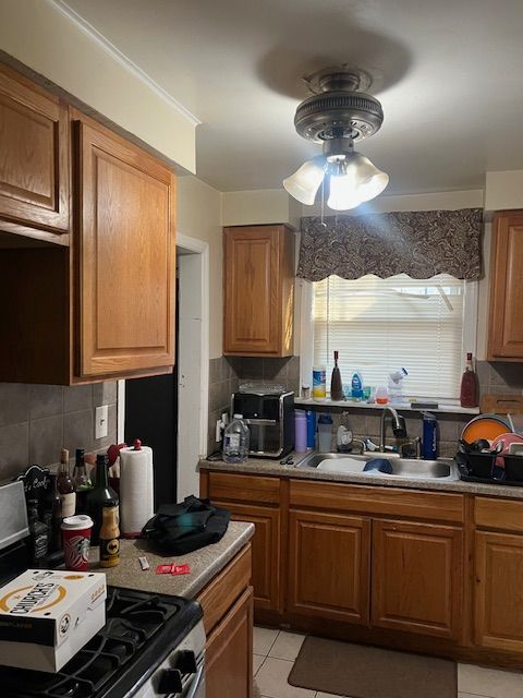 kitchen with backsplash, stove, a sink, and brown cabinets