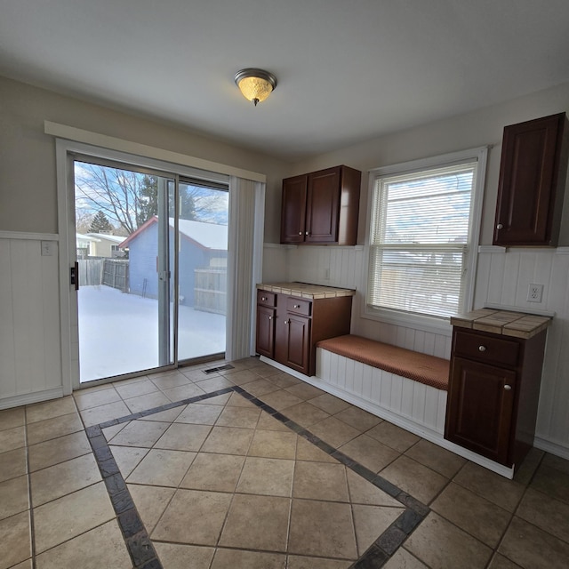 kitchen with a wainscoted wall, a healthy amount of sunlight, dark brown cabinetry, and visible vents