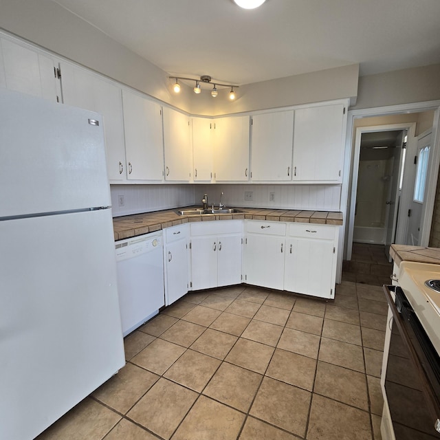 kitchen with light tile patterned floors, decorative backsplash, white cabinetry, a sink, and white appliances