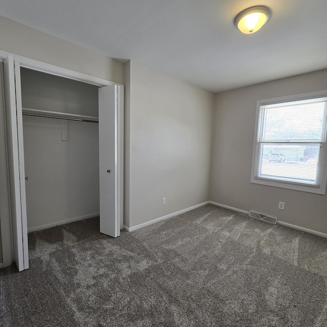 unfurnished bedroom with dark colored carpet, a closet, visible vents, and baseboards