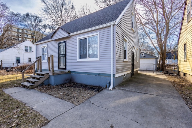 view of front facade with a detached garage, fence, an outdoor structure, concrete driveway, and a shingled roof