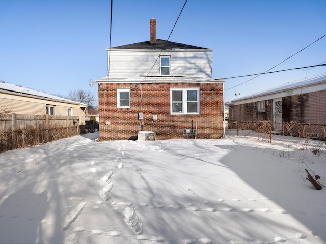 snow covered property with brick siding and fence