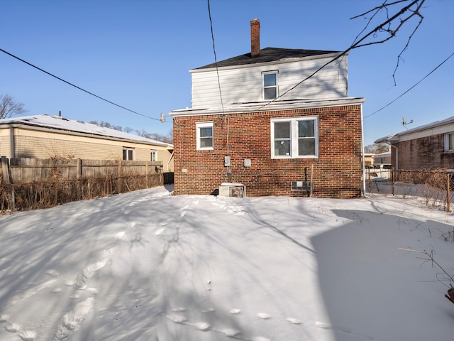 snow covered property featuring brick siding, a chimney, and fence