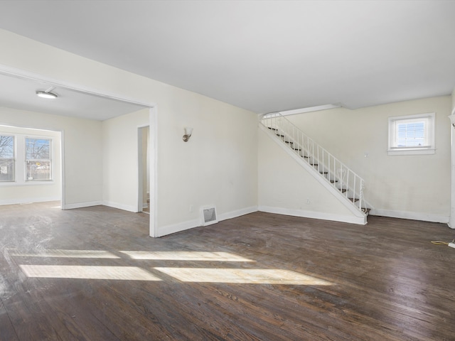 unfurnished living room featuring dark wood-type flooring, visible vents, baseboards, and stairs