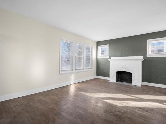 unfurnished living room featuring wood finished floors, plenty of natural light, a fireplace with flush hearth, and baseboards